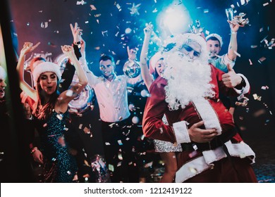 Man in Santa Claus Costume on New Year Party. Happy New Year. People Have Fun. Indoor Party. Celebrating of New Year. Young Women in Dresses. Young Men in Suits. Happy People. Man with White Beard. - Powered by Shutterstock
