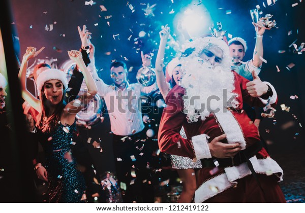 Man in Santa Claus Costume on New Year Party.\
Happy New Year. People Have Fun. Indoor Party. Celebrating of New\
Year. Young Women in Dresses. Young Men in Suits. Happy People. Man\
with White Beard.