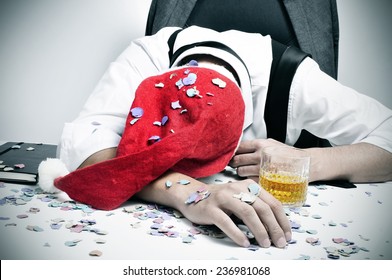 A Man With A Santa Hat And Covered With Confetti Sleeping In His Desk After An Office Christmas Party