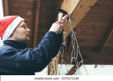 man with santa hat decorating house outdoor carport. installing christmas lights