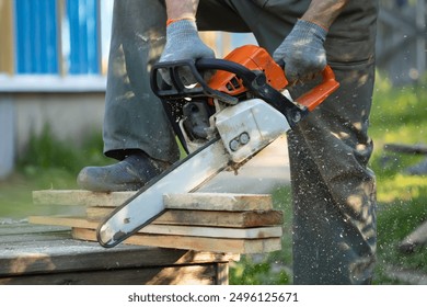 A man sawing boards with a chainsaw. A man sawing with a chainsaw. Red chainsaw. Sawing boards. Sawdust flying from cutting boards with a chainsaw.