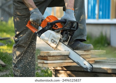 A man sawing boards with a chainsaw. A man sawing with a chainsaw. Red chainsaw. Sawing boards. Sawdust flying from cutting boards with a chainsaw. cutting wood with a motor saw - Powered by Shutterstock