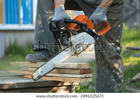 A man sawing boards with a chainsaw. A man sawing with a chainsaw. Red chainsaw. Sawing boards. Sawdust flying from cutting boards with a chainsaw.