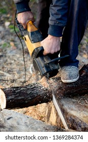 A Man Is Sawing A Log With An Electric Saw, Wood Chips Are Flying