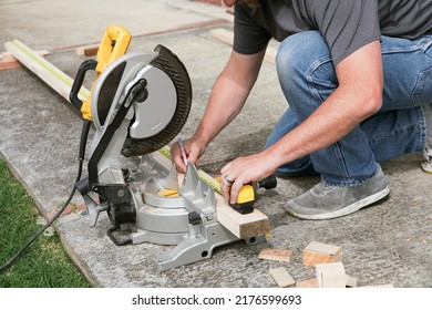 A man sawing wood with a multi material construction saw on the ground and using measuring tape. - Shutterstock ID 2176599693