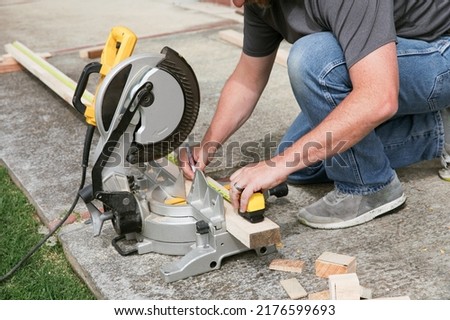 A man sawing wood with a multi material construction saw on the ground and using measuring tape.