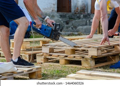 A Man Sawing A Wooden Pallet With A Chainsaw. Making Outdoor Furniture From Pallets