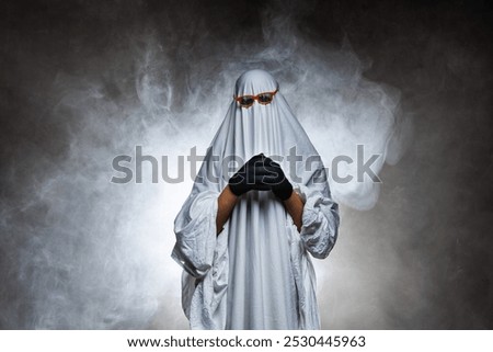 man in scary ghost costume in smoke on grey mysterious background in studio. Minimal halloween ghost concept.