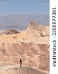 Man with scenic view of summit peak Manly Beacon seen from Zabriskie Point, Badlands, Furnace creek, Death Valley National Park, California, USA. Erosional landscape of Amargosa Chaos rock formation