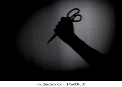 man with scissors silhouette over dark wall. black and white photo can be used for illustrating horror and violence attack. crime concept. simple. selective focus. blurred.