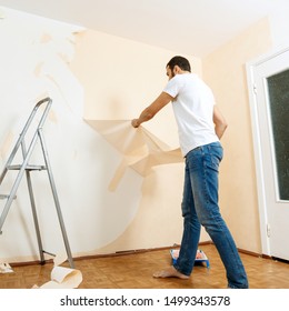 Man in with a scraper in the process of removing old wallpaper. Preparing the wall for sticking new wallpaper.