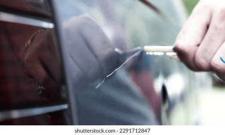 Man scratching car paint with key. Vandalism, blurred background