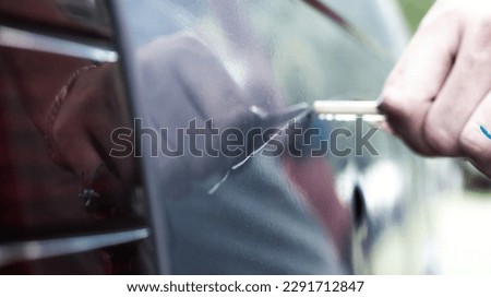 Man scratching car paint with key. Vandalism, blurred background