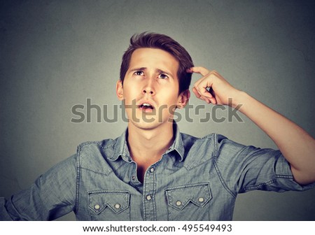 Man scratching head, thinking about something, looking up, isolated on grey wall background. Human facial expression, emotion, feeling