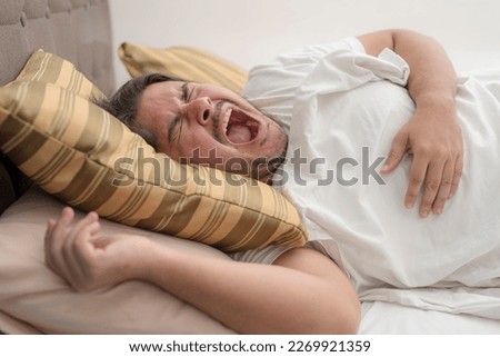 A man screams due to excruciating pain while lying on the bed. An severe bout of heartburn or GERD.