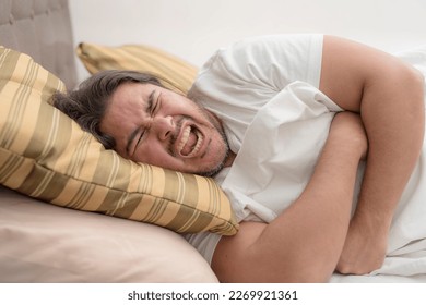 A man screams while clutching his ribcage while resting on his side on the bed. Possible pulled muscle or rib fracture.