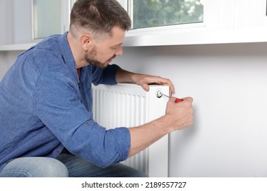 Man With Screwdriver Fixing Radiator At Home