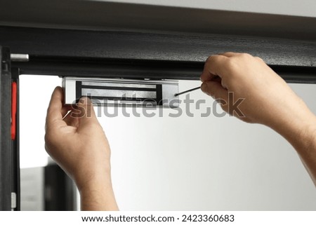 Man with screwdriver installing electromagnetic door lock indoors, closeup. Home security