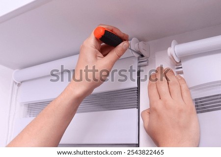 Man with screwdriver installing roller blinds on window