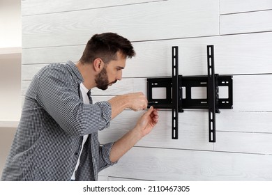 Man With Screwdriver Installing TV Bracket On Wall Indoors