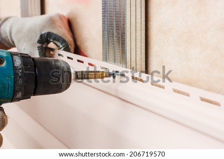 man screws in a wall using an electric screwdriver, attaching siding to metal construction
