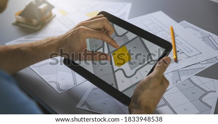 man searching building plot to buy on cadastral plan for house construction on digital tablet