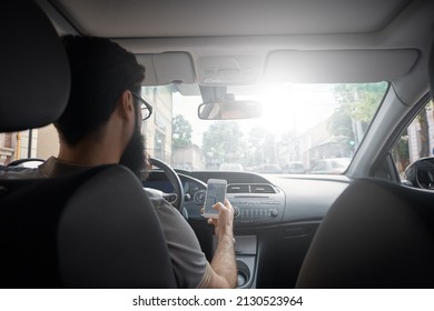 Man Searching Destination Direction Or Address On Gps Or Navigator Application Via Mobile Smartphone Inside A Car While Driving Car - Back View. Technology, Distraction And Driving Concept