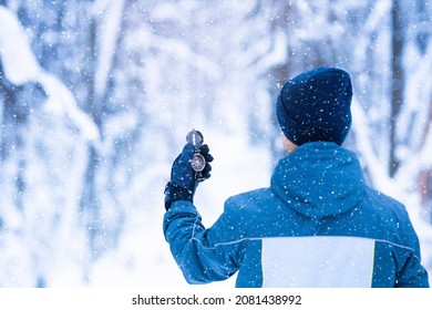 Man is searching for right direction using compass in winter forest in snow storm