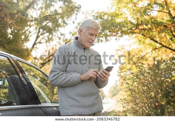 Man searching something at the smartphone while\
standing near his car