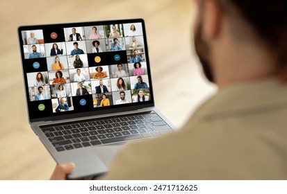 A man is seated in front of a laptop, where a screen displays a video call with multiple people. He appears focused and engaged as he interacts with the group virtually. - Powered by Shutterstock