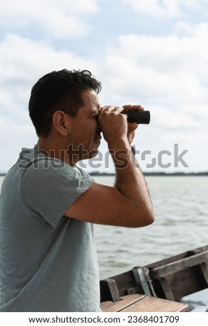 A man seated on a boat, sailing on a calm sea while looking ahead through a spyglass