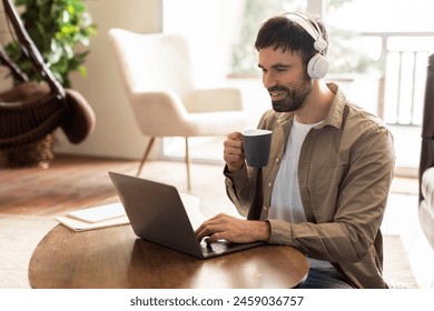 A man is seated at a table, focused on his laptop screen. Next to him is a cup of coffee, steam rising. The mans hands are typing on the keyboard as he works. - Powered by Shutterstock