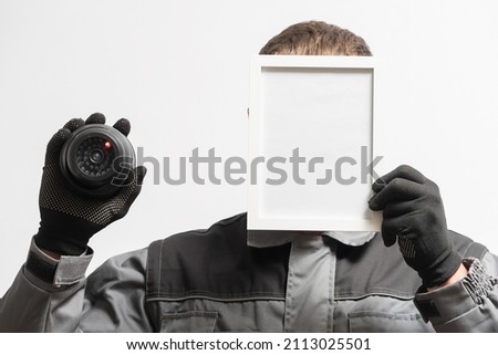 A man with the security cctv camera is hiding his face behind the blank photo frame with copy space. Privacy concept.