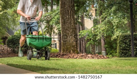 Man seeding and fertilizing residential backyard lawn with manual grass seed spreader.