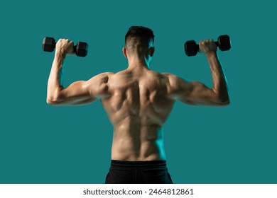 A man is seen from the back performing a shoulder press with dumbbells in each hand. His muscular back is highlighted against a solid teal background - Powered by Shutterstock