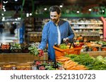 Man selecting fresh vegetables in grocery store, holding orange basket, surrounded by vibrant produce. Concept of healthy lifestyle and eco-friendly shopping in local market. Focus fresh food choice