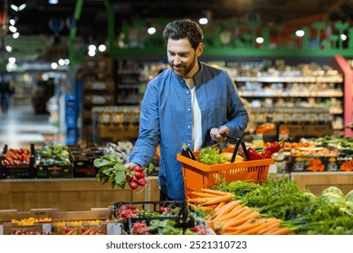 Man selecting fresh vegetables in grocery store, holding orange basket, surrounded by vibrant produce. Concept of healthy lifestyle and eco-friendly shopping in local market. Focus fresh food choice - Powered by Shutterstock