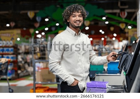 Man at a self-checkout terminal in a store, utilizing a smartphone for payment.