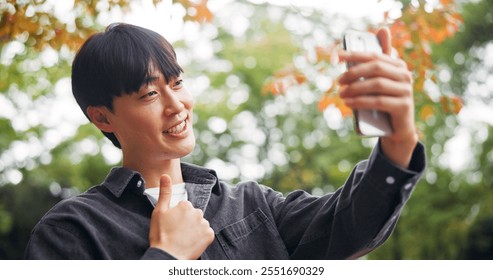 Man, selfie and outdoor with thumbs up for social media, video call and connectivity in Tokyo. Japanese person, smile and like emoji in park for photography, live streaming or approval vote for app - Powered by Shutterstock