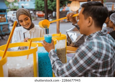 man sells colorful drink and juice in a jar to his female customer. street food vendor - Powered by Shutterstock