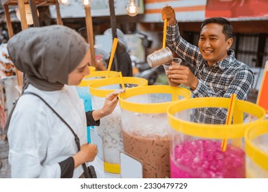 man sells colorful drink and juice in a jar to his female customer. street food vendor - Powered by Shutterstock