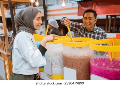 man sells colorful drink and juice in a jar to his female customer. street food vendor - Powered by Shutterstock