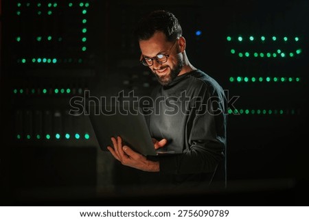 Man in server room interacting with servers using laptop. Maintaining data center infrastructure and cybersecurity