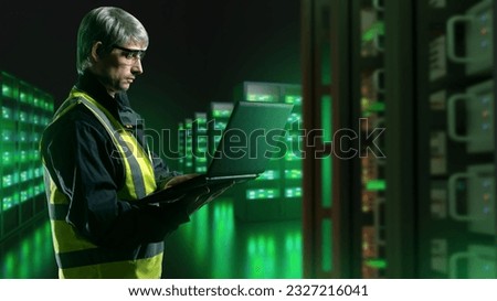 Man in server room. System administrator with laptop. Guy works for hosting company. Data center. Man controls server equipment. Engineer sets up server hardware. Telecommunications, internet