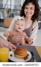 Man Serving Pancakes To Cheerful Wife With Infant Daughter During Breakfast