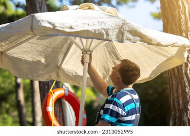 A man sets up a big sun umbrella for his family beach. - Powered by Shutterstock