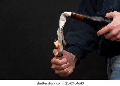 A man sets fire to a Molotov cocktail on a dark background, close-up, selective focus.