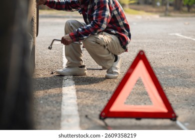 A man sets up a reflective triangle to warn other drivers to be careful of cars parked on side of the road. A man sets up an orange reflective triangle on the side of the road to change a flat tire.