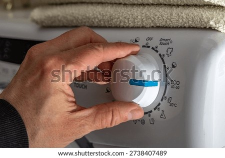 A man sets the washing program on the thermostat of an automatic washing machine, an eco-friendly program that saves energy and water, the thermostat knob of an automatic washing machine, high water consumption during washing
