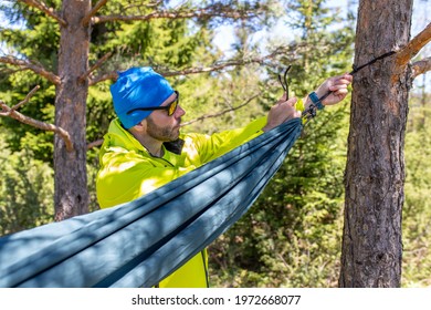 Man is setting up a hammock between two trees in the mountain.